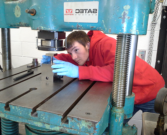 Person in a red hoodie 和 blue gloves works with a metal machine